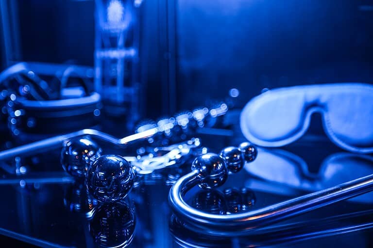 Dunkle BDSM-Accessoires mit blauer Beleuchtung, einschließlich Augenbinde, Ketten und peitsche, für professionelle Spiele.