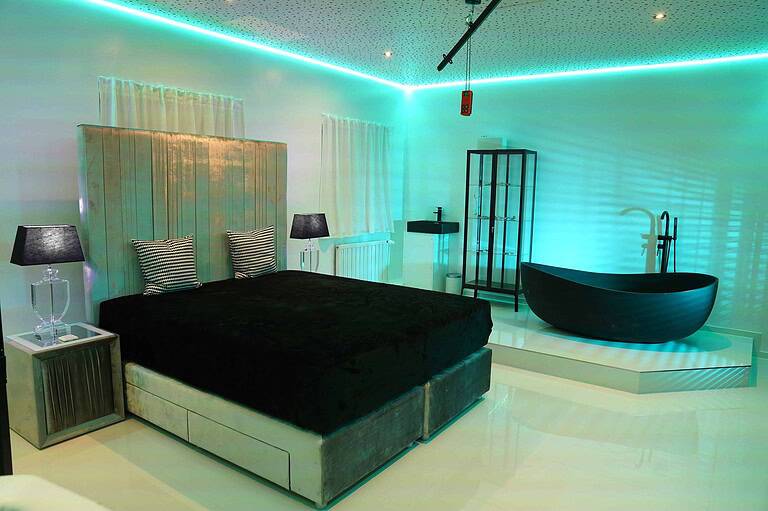 Modernes Schlafzimmer mit dunklem Bett und Rosa Lichtatmosphäre.