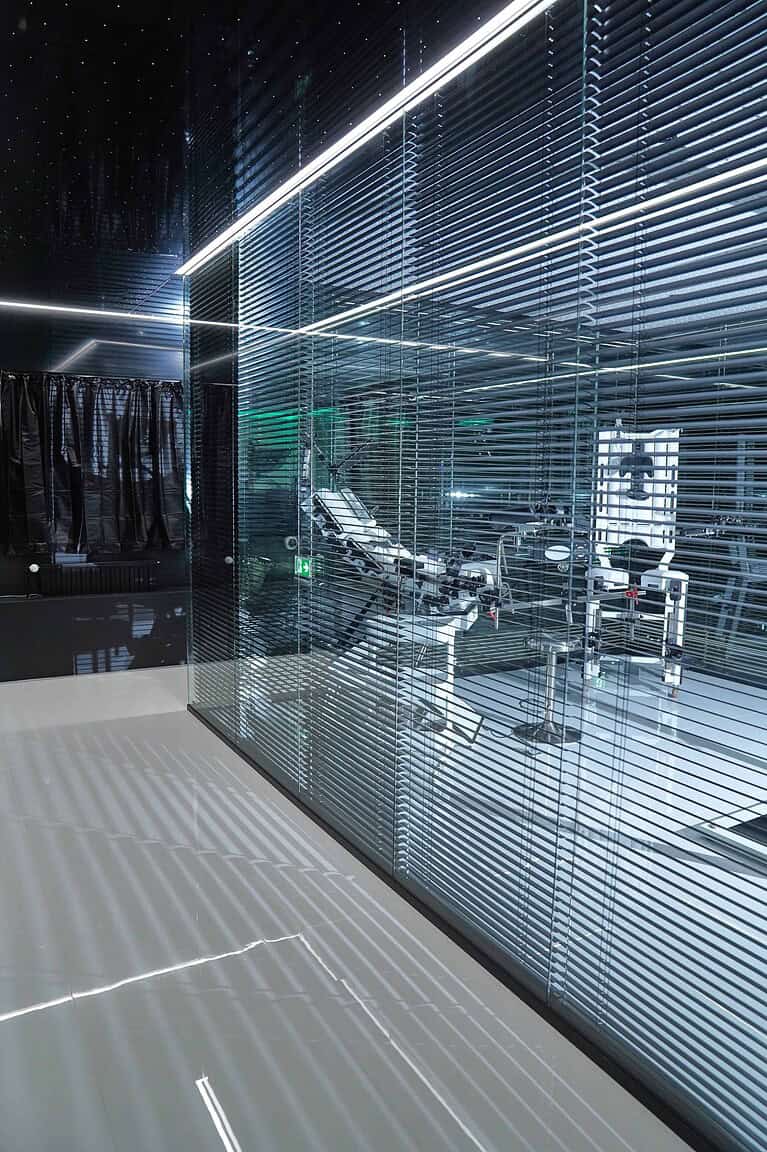 Hinter Glaswänden im BDSM Hotel München, stilvoller Studio mit modernen BDSM-Equipment.