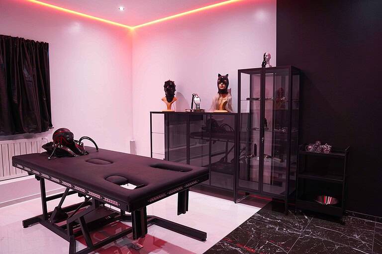 Hochwertiger BDSM Raum mit Massagebank und Masken.