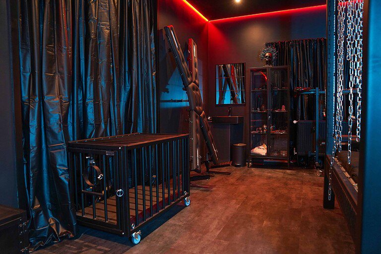 Luxus BDSM Studio München mit stilvoller Einrichtung, Lederspielzeugen, Käfig und dunklem Ambiente.