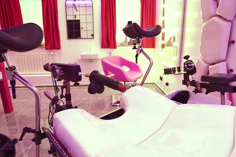 Dunkler BDSM Raum in München mit Velokurb, Bondage-Stationen und roter Beleuchtung, ideal für exklusive Fetisch-Events.