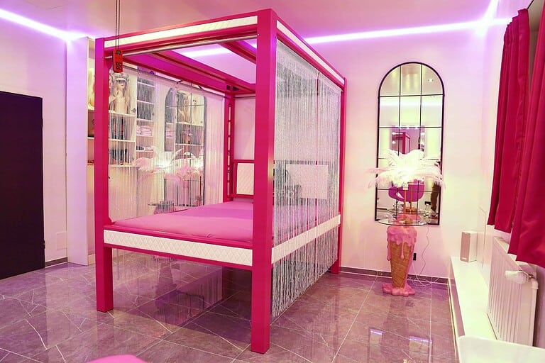 Moderne BDSM Hotelzimmer mit pinkem Bett und stilvoller Einrichtung.