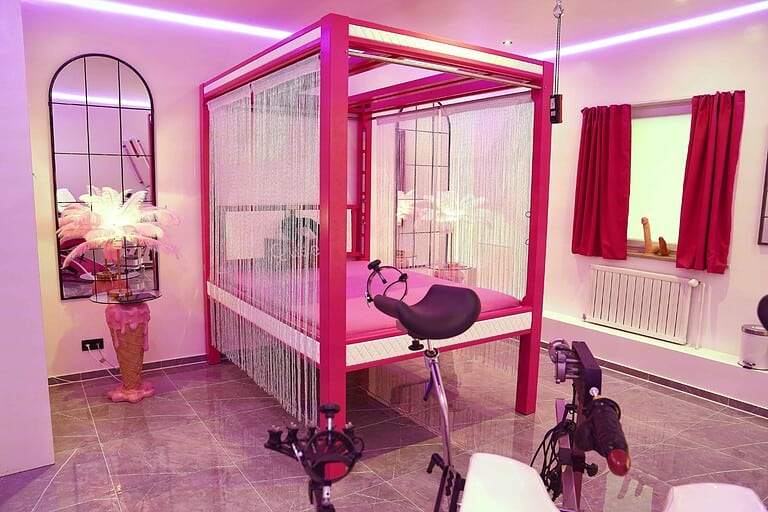 Innenraum eines BDSM Hotelzimmers in München mit pinkem Bett und Trennvorhängen.